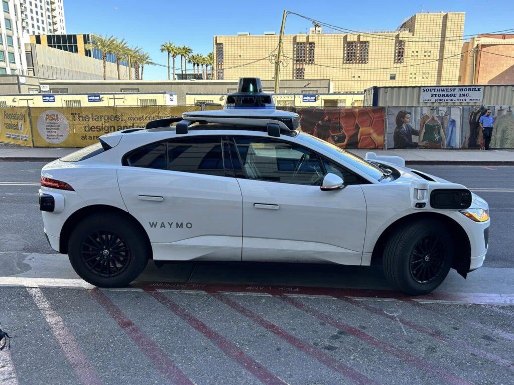 A driverless Waymo car arrives curbside in Arizona, ready to pick up a passenger.