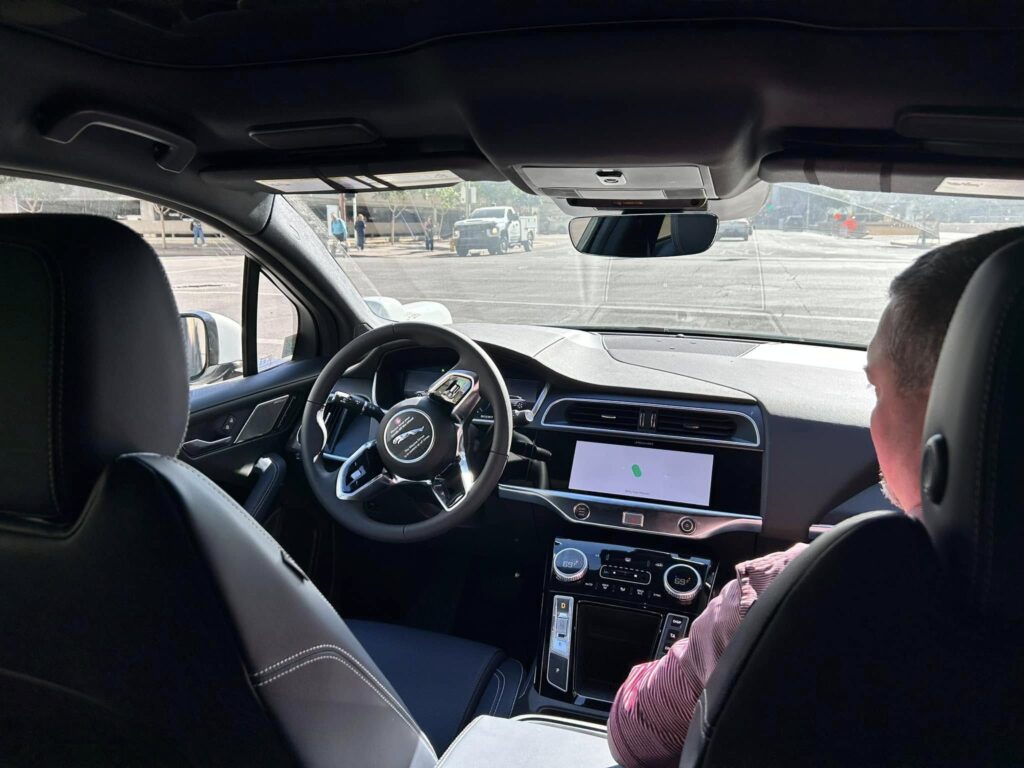 Pat sits in the passenger seat of a driverless Waymo vehicle, looking over as the car navigates autonomously.