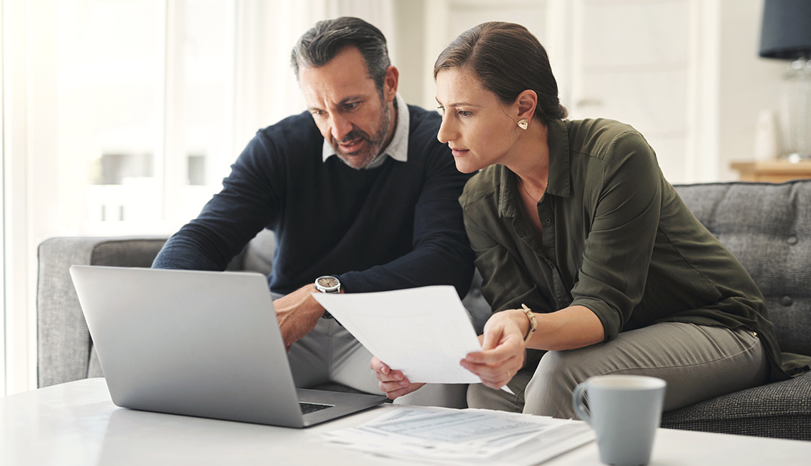 Mature couple sitting on a couch with a laptop and financial documents, discussing their retirement plans.